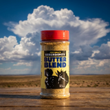 A bottle of Jess Halls Serendipity Butter Blend seasoning stands on a wooden surface with a dramatic blue sky and large white clouds in the background.